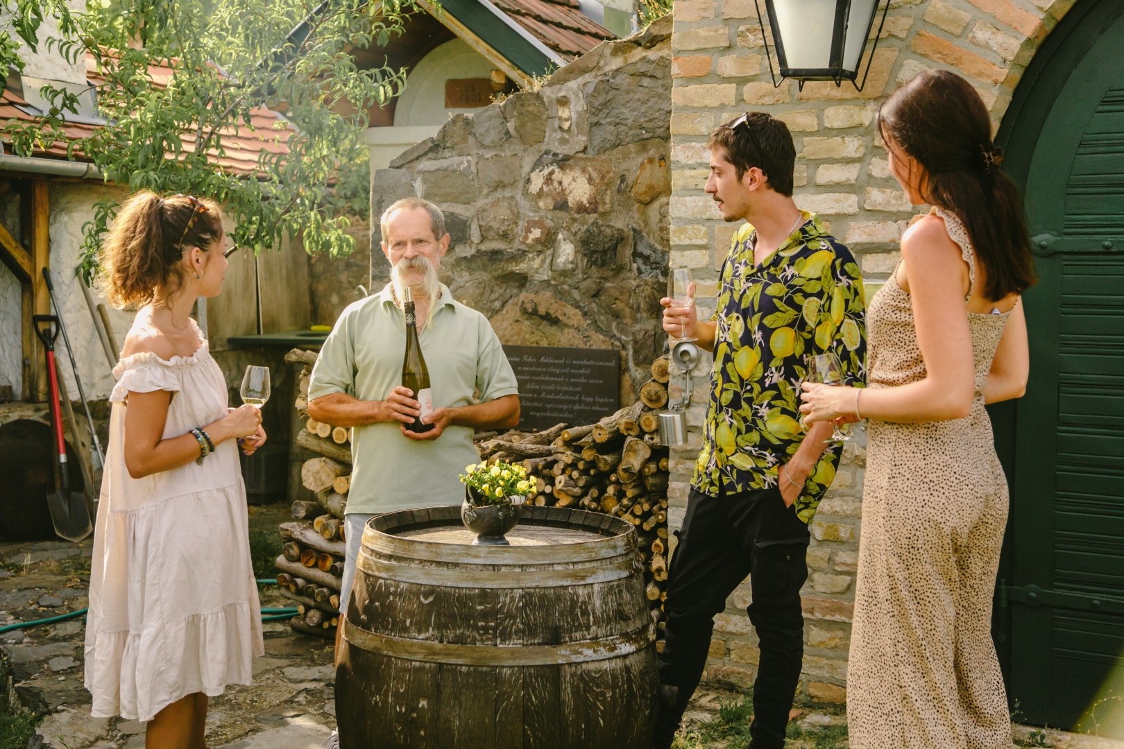 Winemaker presenting a bottle of wine to three visitors during an outdoor tasting in the courtyard of Nyári Winery, Hungary.
