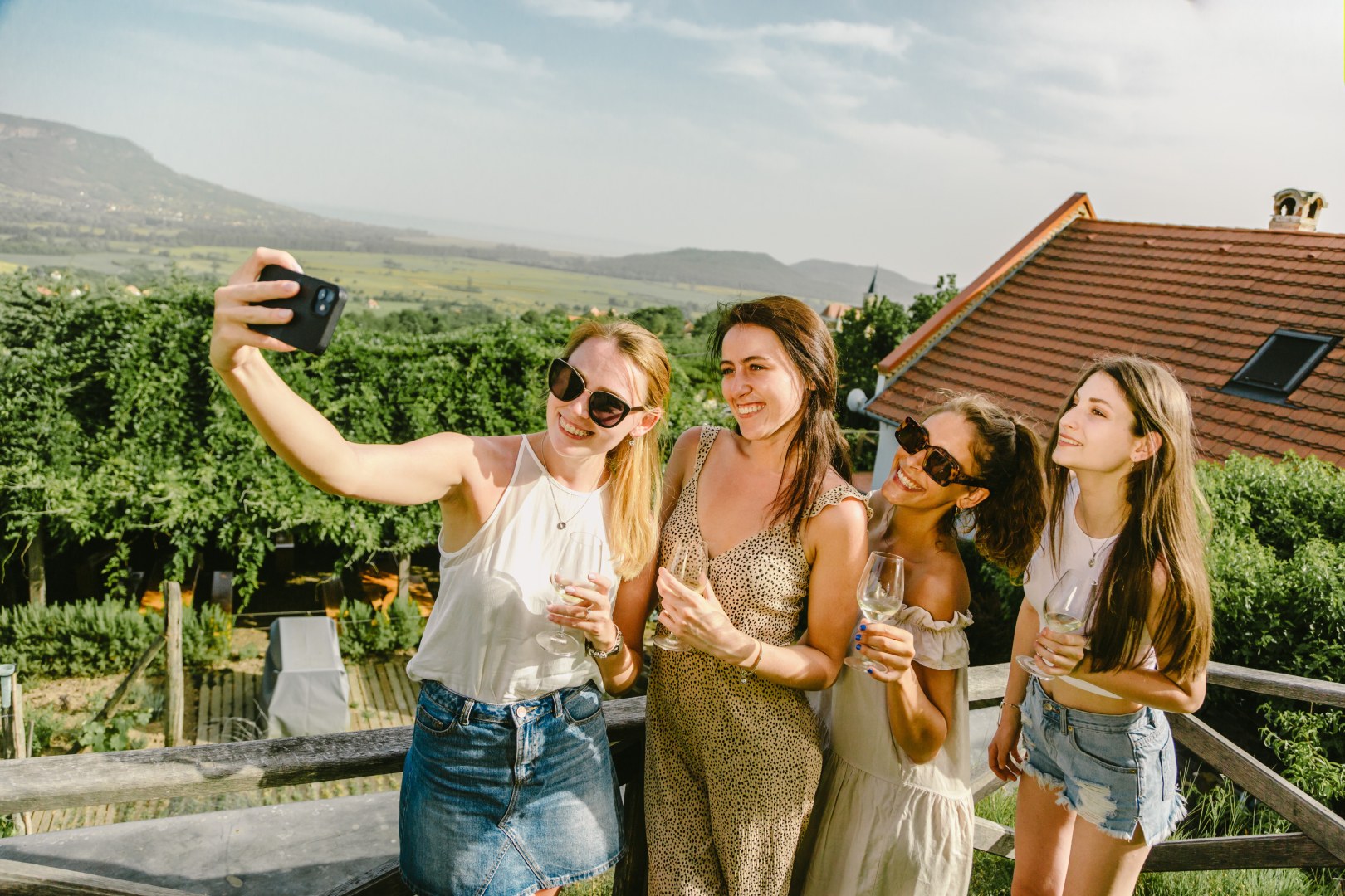 Four women taking a selfie with wine glasses on a vineyard terrace at Nyári Winery, overlooking the volcanic hills of the Balaton Uplands.