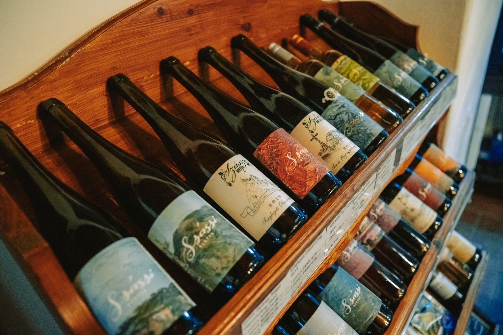 Selection of Szászi Winery wine bottles displayed on wooden shelves in the Badacsony wine region, Hungary.